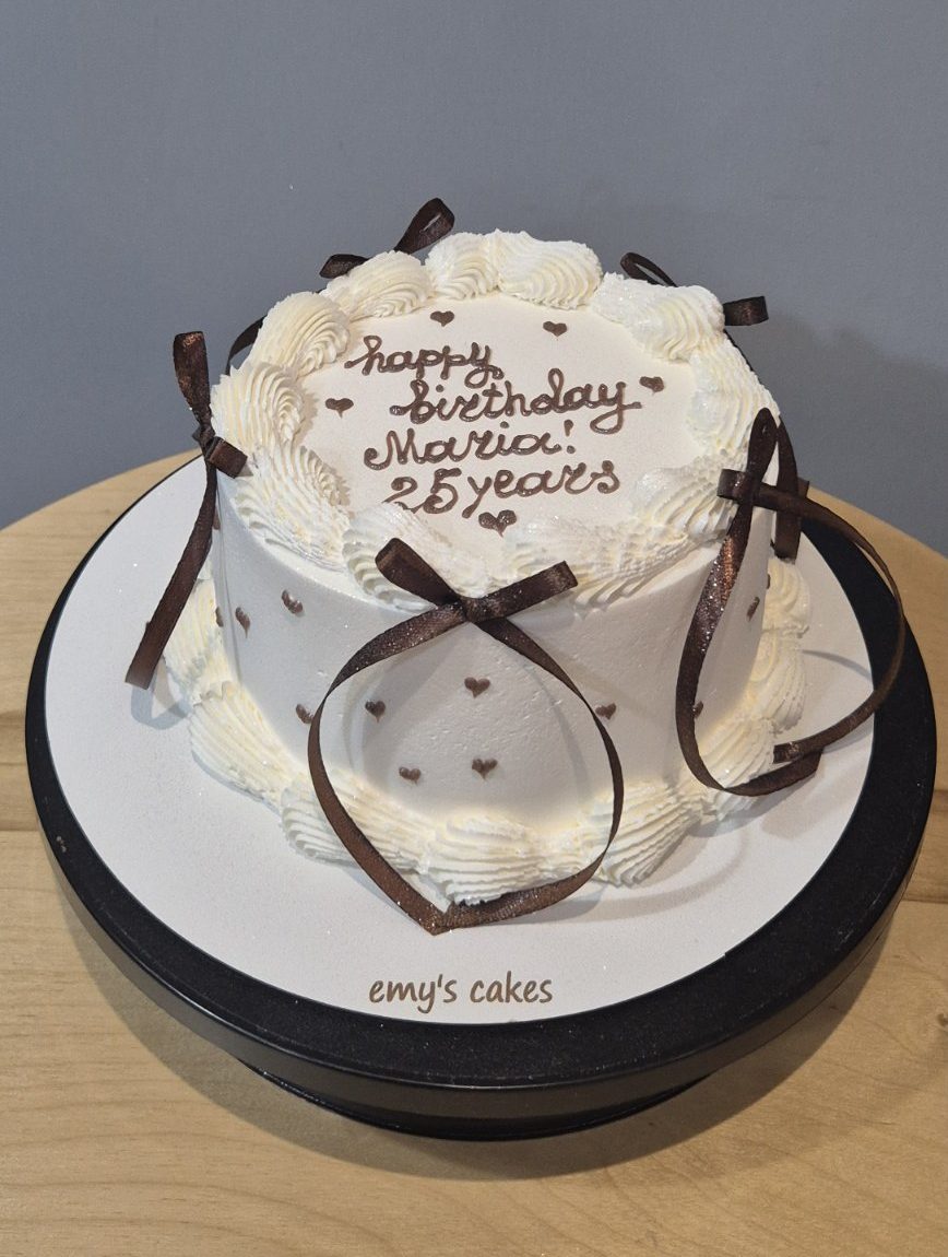 Tort alb acoperit în cremă, fundițe maro, mesaj Happy Birthday și inimioare