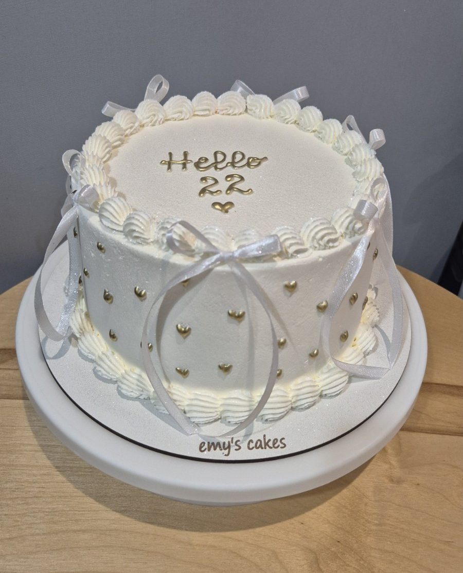 Tort alb cu cremă de brânză, inimioare aurii și fundițe albe, mesaj „Hello 22”