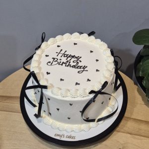 Tort alb cu cremă de brânză, mesaj „Happy Birthday”, inimioare negre și panglici negre