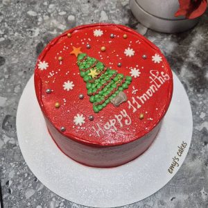 Tort roșu de Crăciun cu brad decorat, fulgi de nea și mesaj „Happy 11 months”