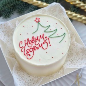 Tort alb de Anul Nou cu brăduț stilizat verde și mesaj rusesc „С Новым годом!”