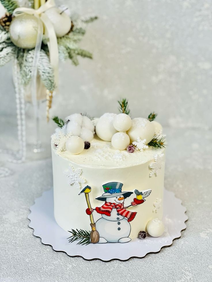 Tort de iarnă acoperit în cremă de brânză, decorat cu bulgări albi, crenguțe de brad și om de zăpadă desenat