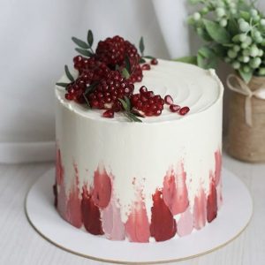 Tort alb elegant cu rodie proaspătă deasupra și pete pictate în nuanțe de roșu pe laterale