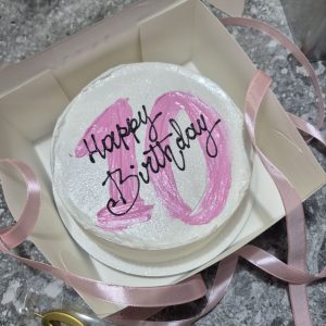 Tort bento alb, cu decor roz în formă de „10” și mesaj „Happy Birthday”, așezat într-o cutie cu panglică roz