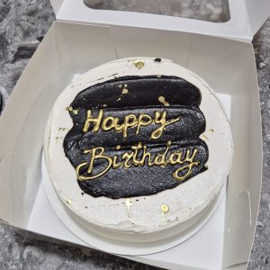Bento cake alb cu decor negru și stropi aurii, cu mesaj „Happy Birthday”, în cutie de cadou, realizat de Emys Cakes.
