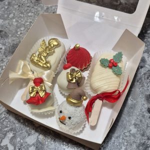 Set de Crăciun cu deserturi asortate în ciocolată albă, decorate festiv cu îngeraș auriu, clopoței, om de zăpadă și frunze de ilex, realizat de Emys Cakes.