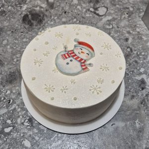 Bento cake alb de Crăciun, acoperit cu velvet sidefat, decorat cu fulgi de zăpadă reliefați și om de zăpadă desenat, realizat de Emys Cakes.