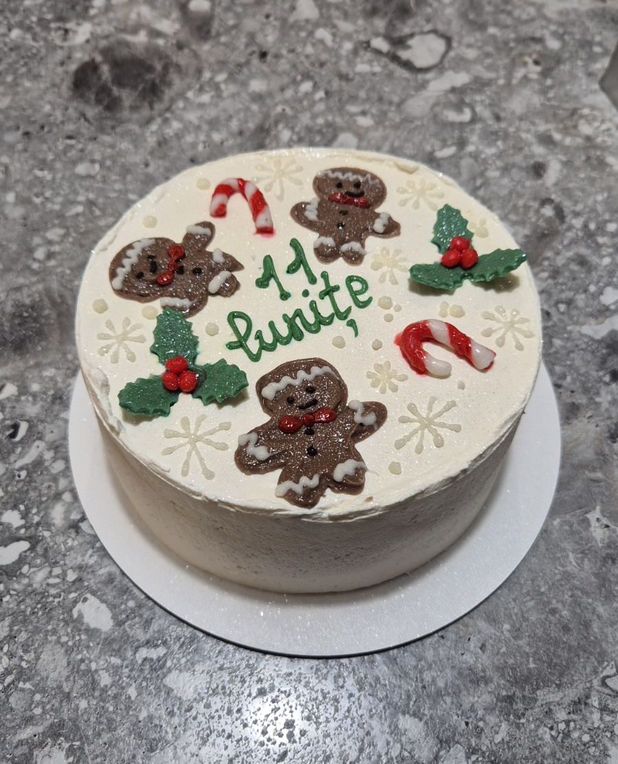 Bento cake alb de iarnă, decorat cu omuleți de turtă dulce, bastonașe „candy cane”, frunze verzi cu bobițe roșii și mesaj „11 lunițe”, realizat de Emys Cakes.