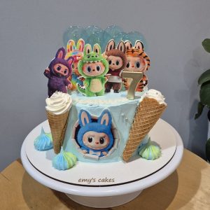 Tort pentru copii acoperit în cremă de brânză albastru pastel, decorat cu personaje haioase în costume de animăluțe, conuri de înghețată, bezele colorate și lumânare cu cifra 7, realizat de Emys Cakes.