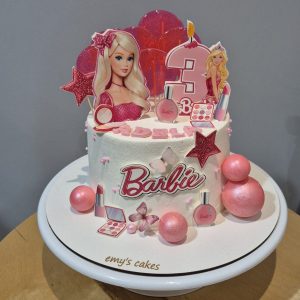 Tort Barbie pentru fetițe, acoperit în cremă de brânză alb-roz, decorat cu păpuși Barbie, bile lucioase, stele sclipitoare, fluturi și cifra 3, realizat de Emys Cakes.