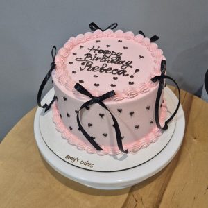 Tort aniversar Rebecca roz cu fundițe negre, inimioare negre, inscripție Happy Birthday Rebecca, cremă brânză, Emys Cakes 2 kg.