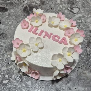 Tort bento cu flori albe și roz, inscripționat „LÎNCA” în roz lucios de la Emys Cakes, decor feminin elegant pentru ocazii speciale