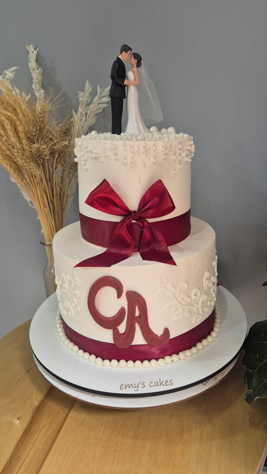 Tort de nuntă alb cu două etaje, figurine miri și fundă burgundy, decor cu perle și inițiale CA, Emys Cakes