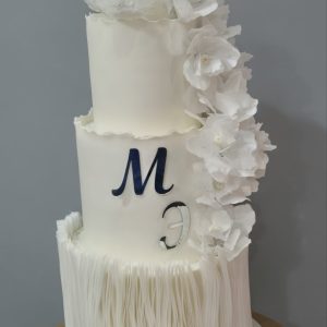 Tort nuntă elegant acoperit în pastă de zahăr albă, cu flori albe și inițiale M&E, decor premium Emys Cakes