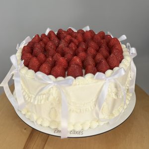 Tort de zi de naștere alb cu multe căpșuni deasupra, fundițe albe pe margine, crem chesse și decor elegant, Emys Cakes