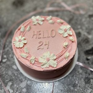 Bento tort roz cu inscripția „HELLO 24” și flori albe decorative, pe fundal cu panglică roz, Emys Cakes